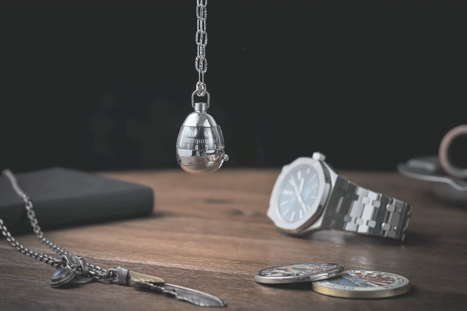 A steel sports watch and a pendant watch resting on a dark timber table