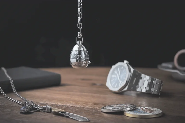 A steel sports watch and a pendant watch resting on a dark timber table