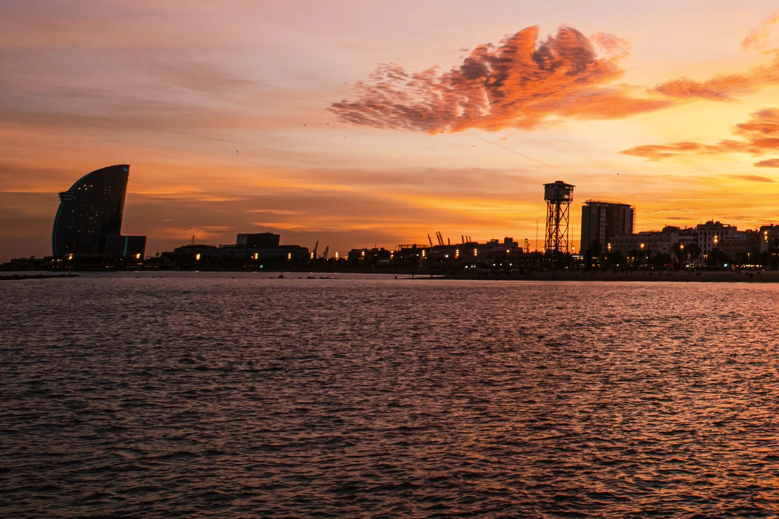 The Barceloneta shore at sunset from the water, the W hotel and the port cable-car tower in silhouette
