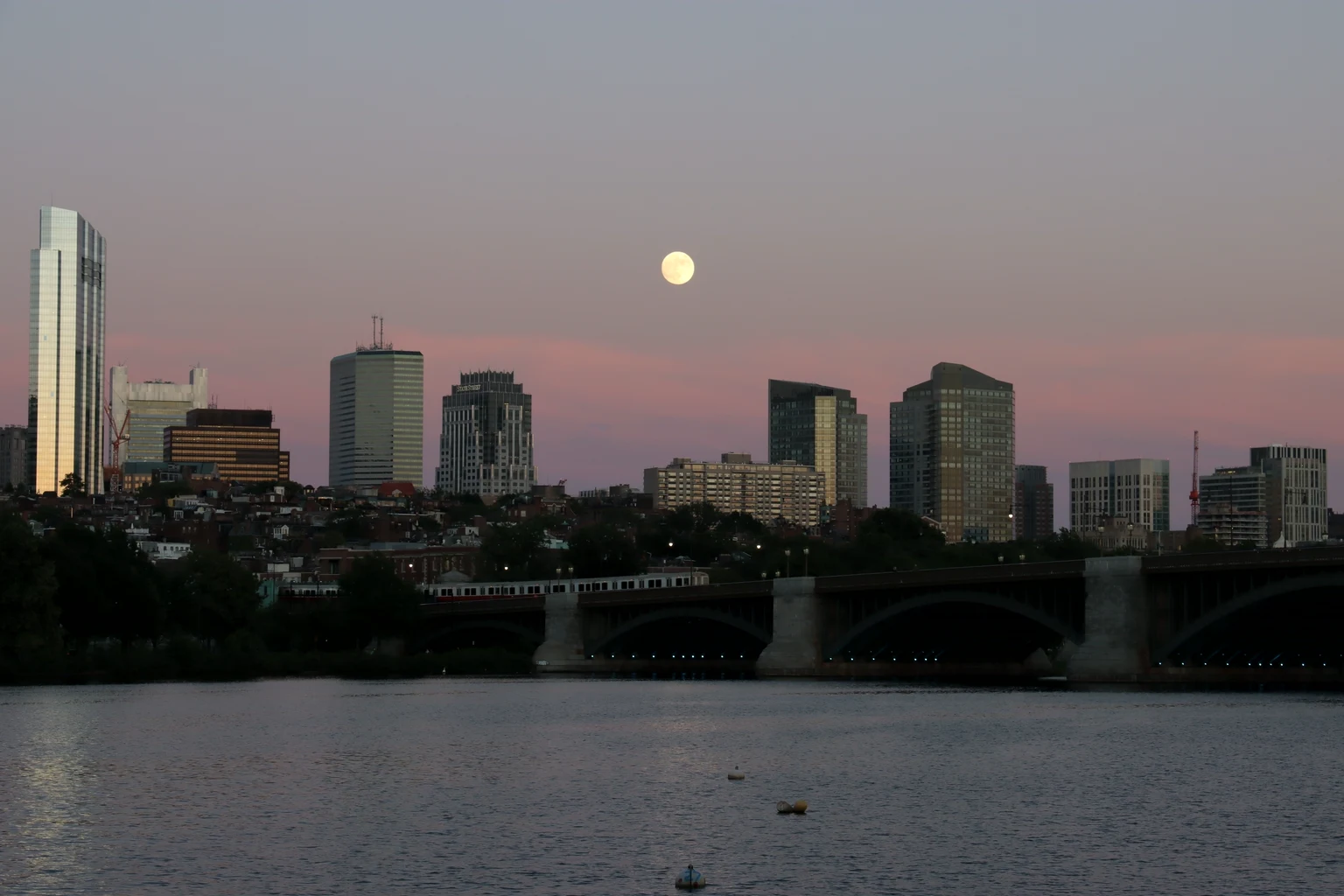 A full moon rising over the Boston skyline and the Charles River at dusk