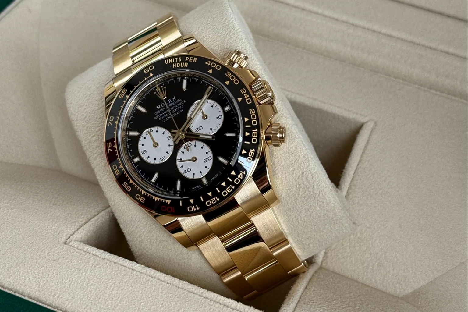 A yellow-gold Rolex Cosmograph Daytona with a black dial and white counters on its cushion inside an open green Rolex presentation box