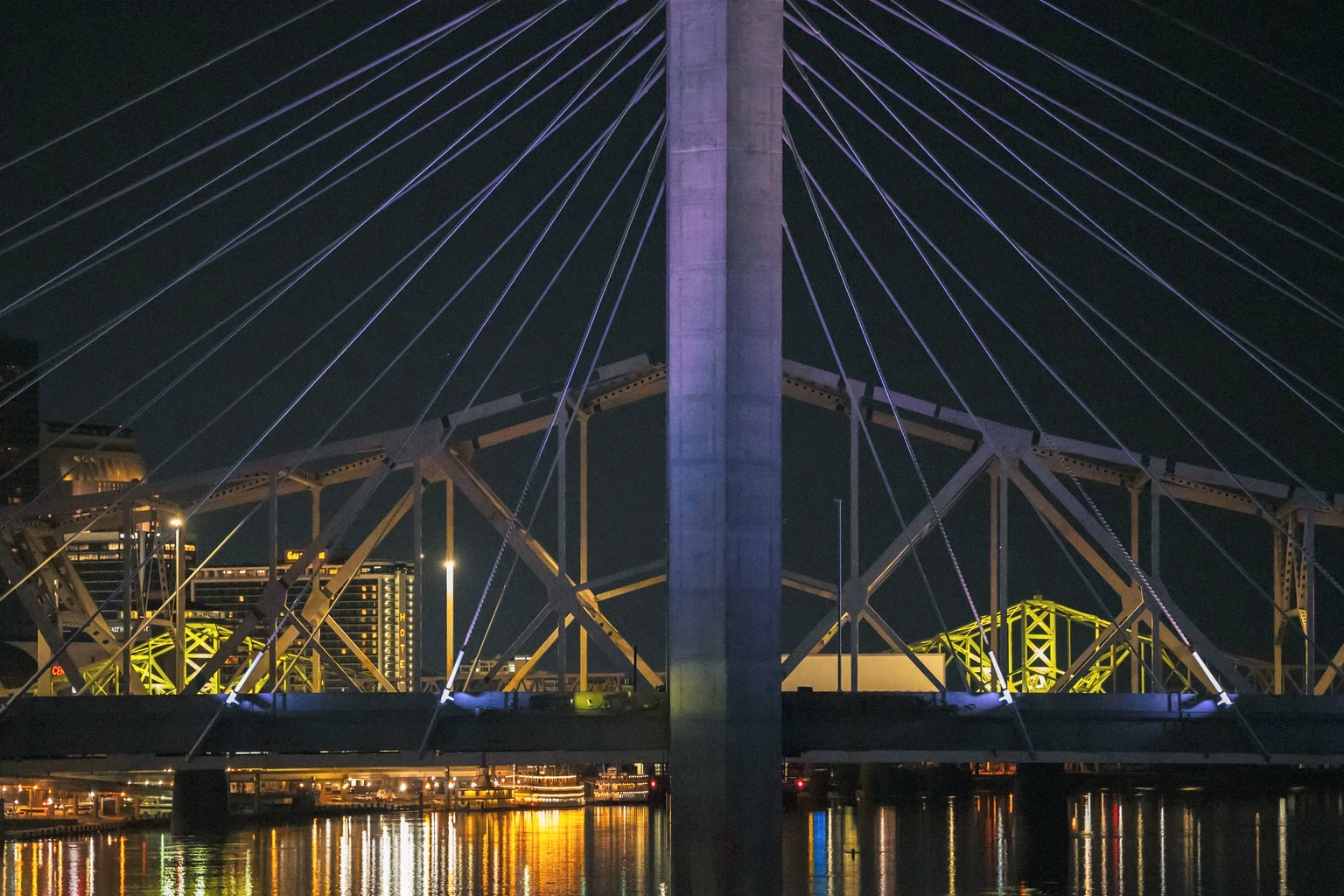 A cable-stayed bridge over the Ohio River at night, downtown Louisville and its riverfront lit behind