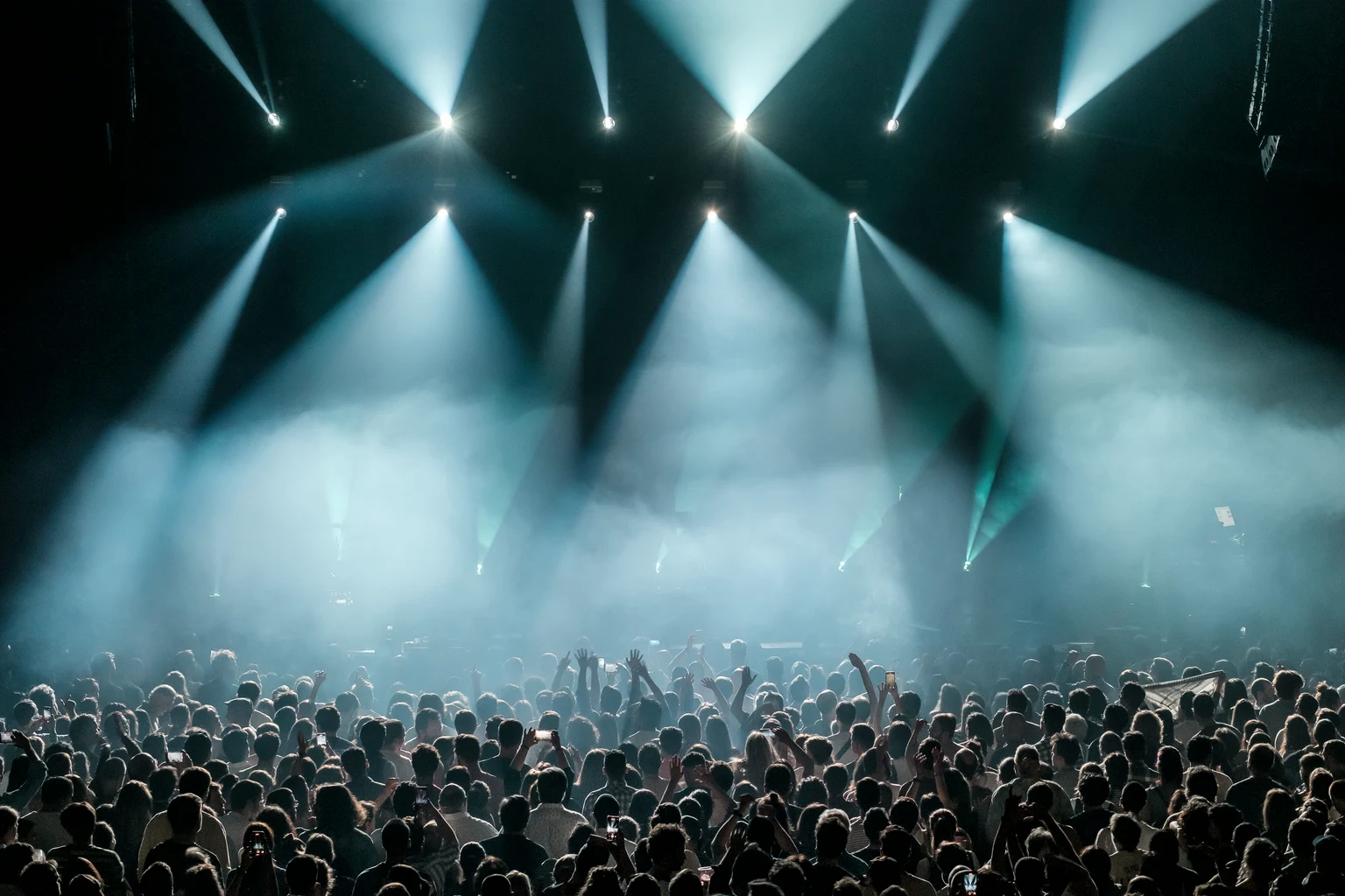 Stage lights beaming over a full arena floor at a concert