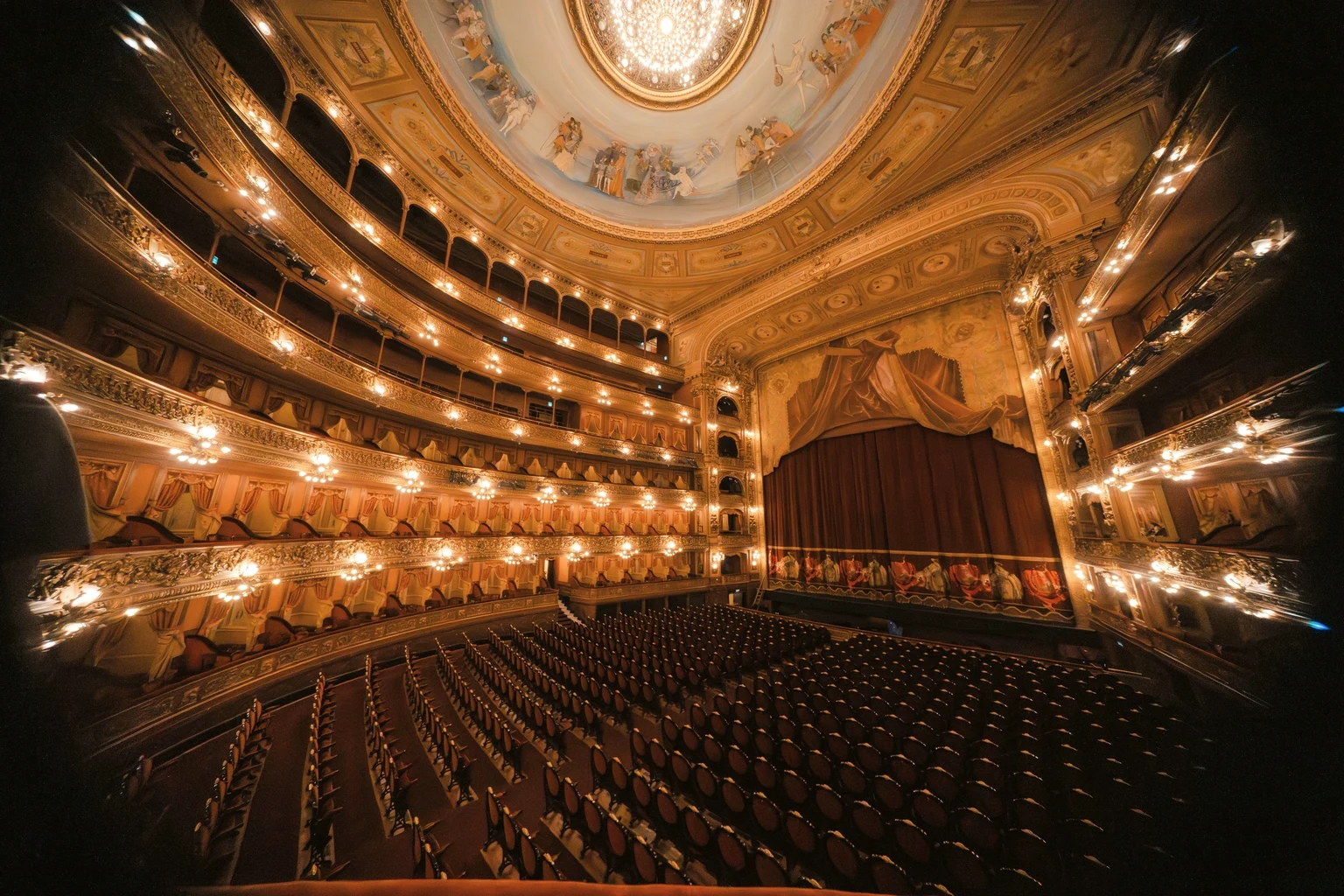 The gilded horseshoe auditorium of the Teatro Colón in Buenos Aires, its tiers of boxes lit and the stage curtain closed