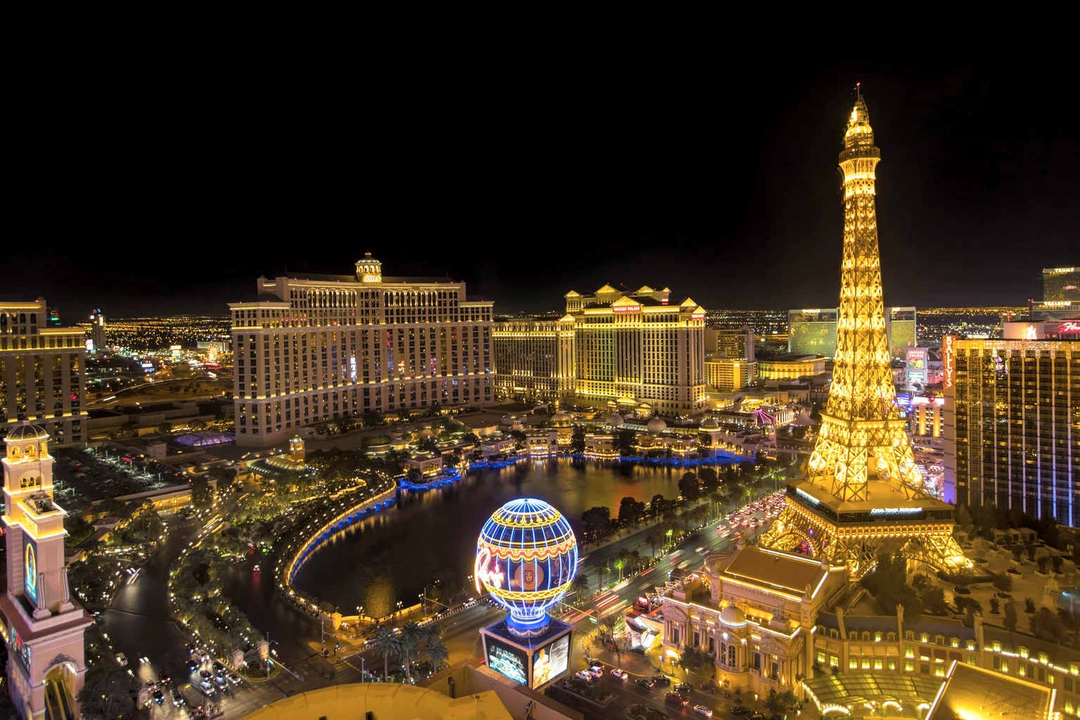 The Bellagio, its lake and Caesars Palace at night, the Paris Las Vegas tower lit gold on the right