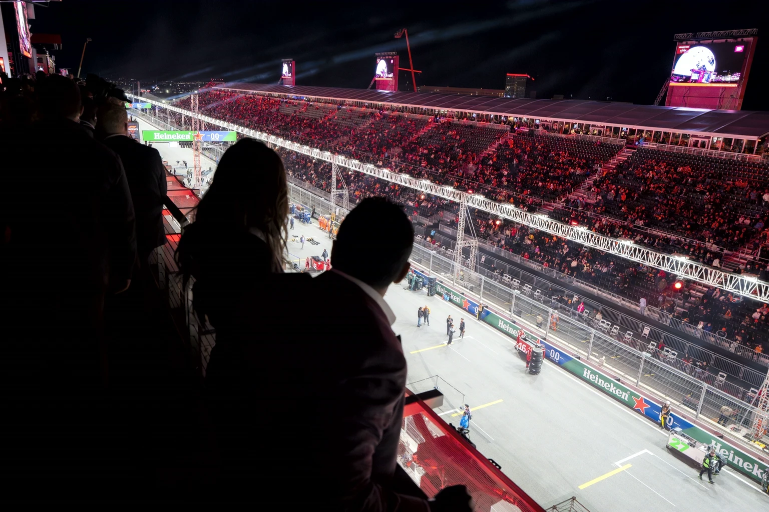 Guests on a hospitality balcony looking down on the start-finish straight and the full grandstand opposite, Las Vegas, at night
