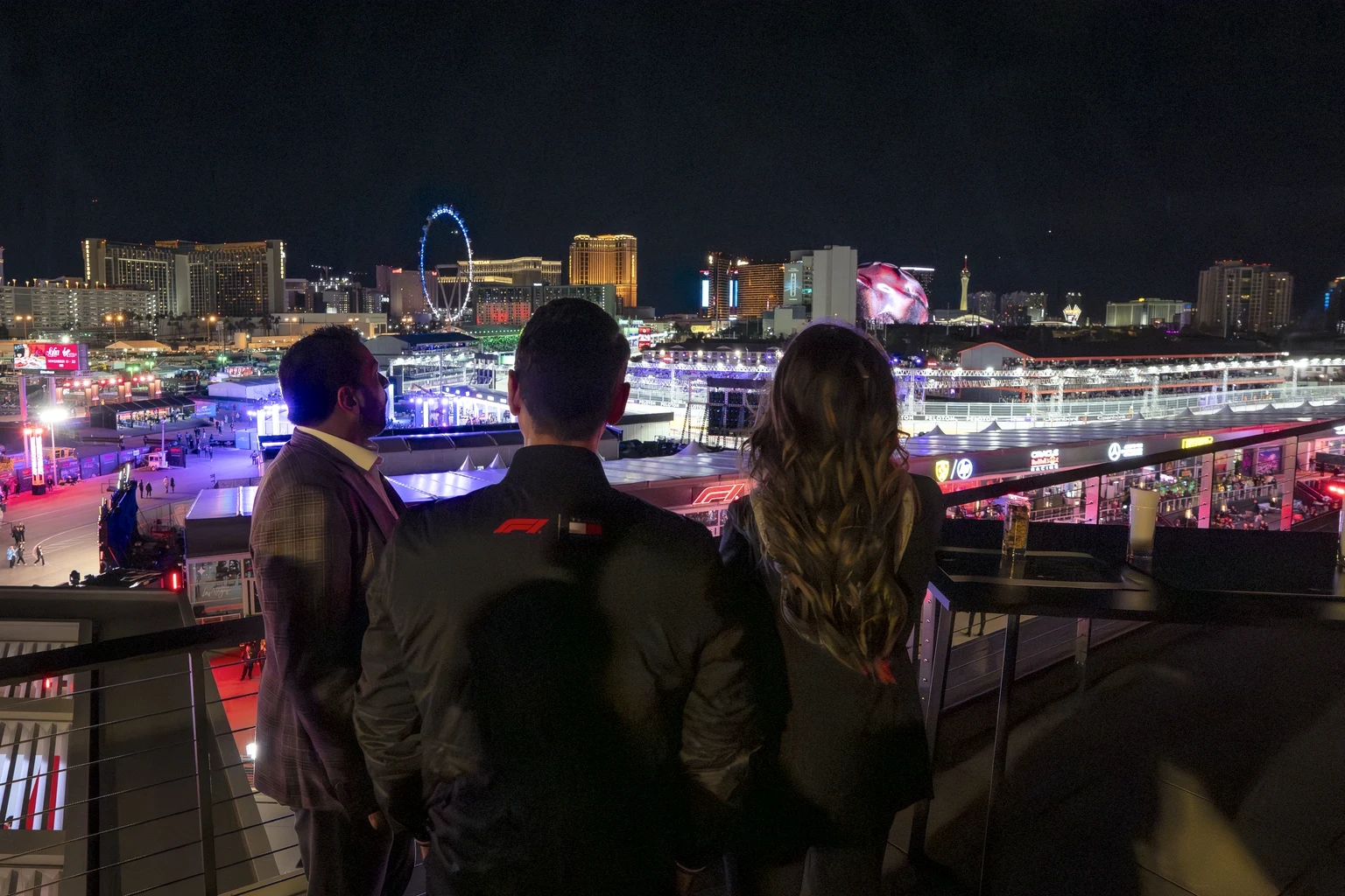 Guests on a hospitality terrace above the Las Vegas Strip Circuit at night, the Strip, the High Roller and the Sphere lit behind