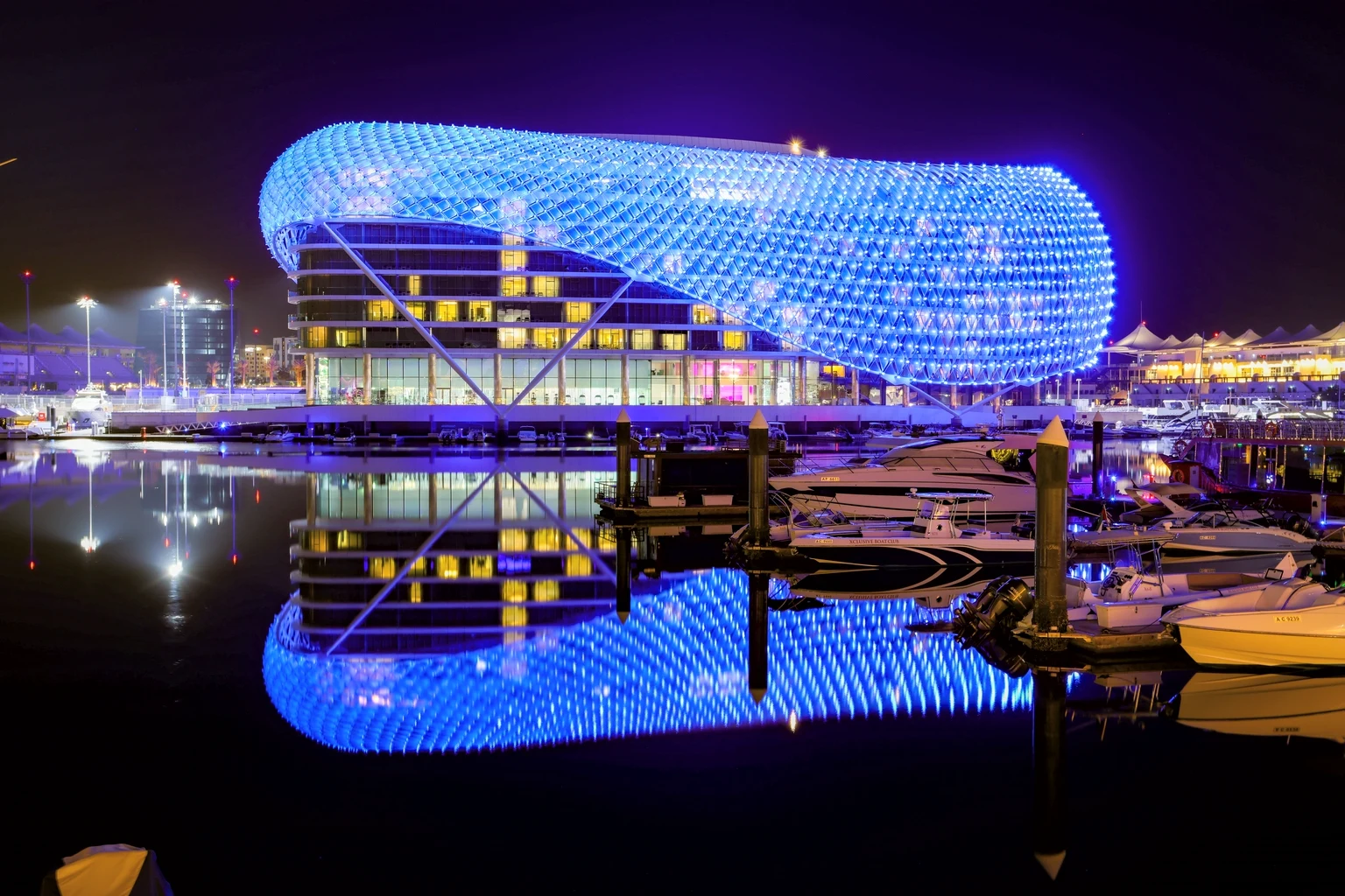 The W Abu Dhabi hotel on Yas Marina at night, its lattice canopy lit blue and reflected in the marina