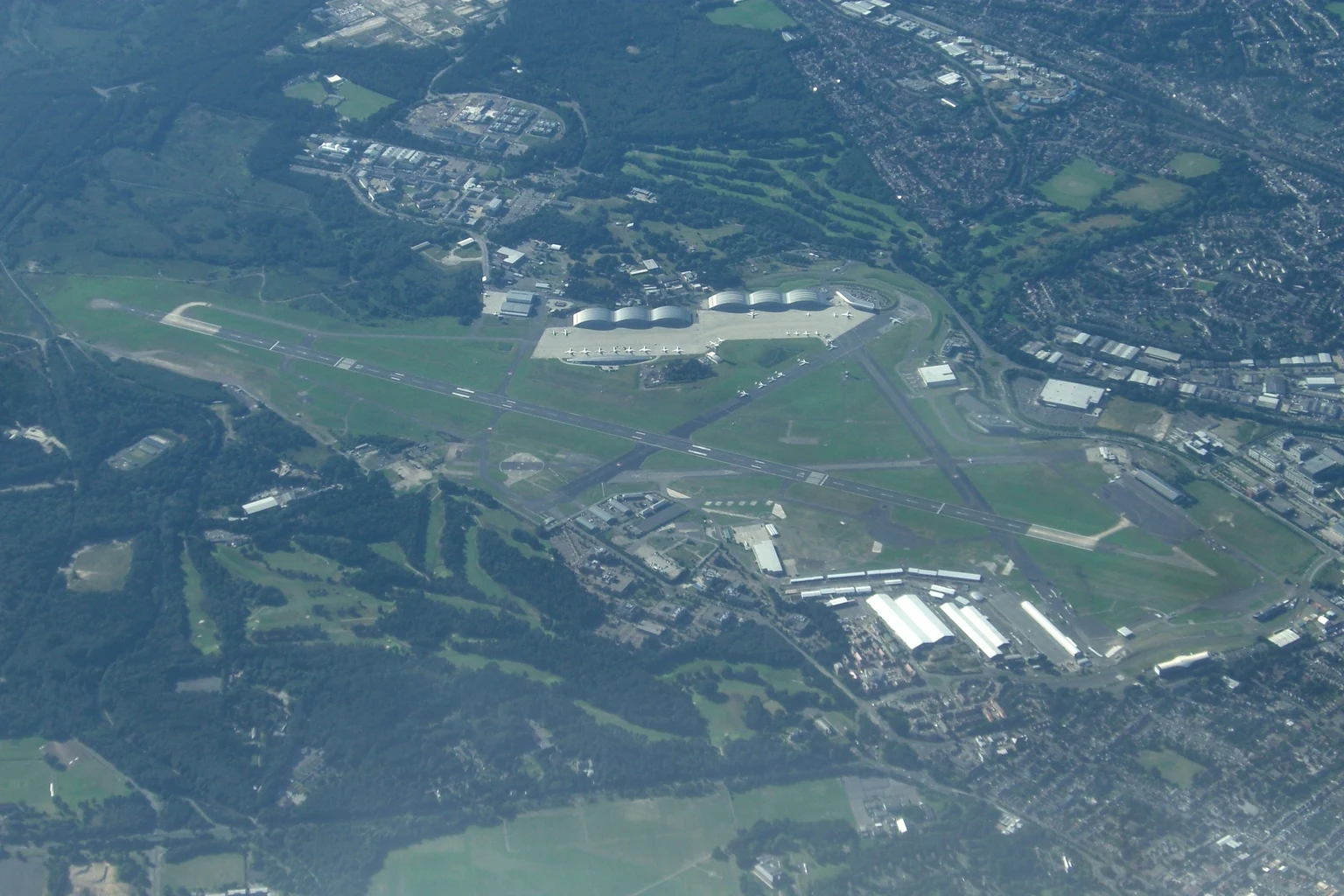 Farnborough Airport from the air: the long runway, the curved roofs of the hangars and the town around it