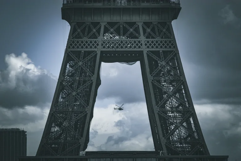 A helicopter flying between the legs of the Eiffel Tower under a dark, stormy sky