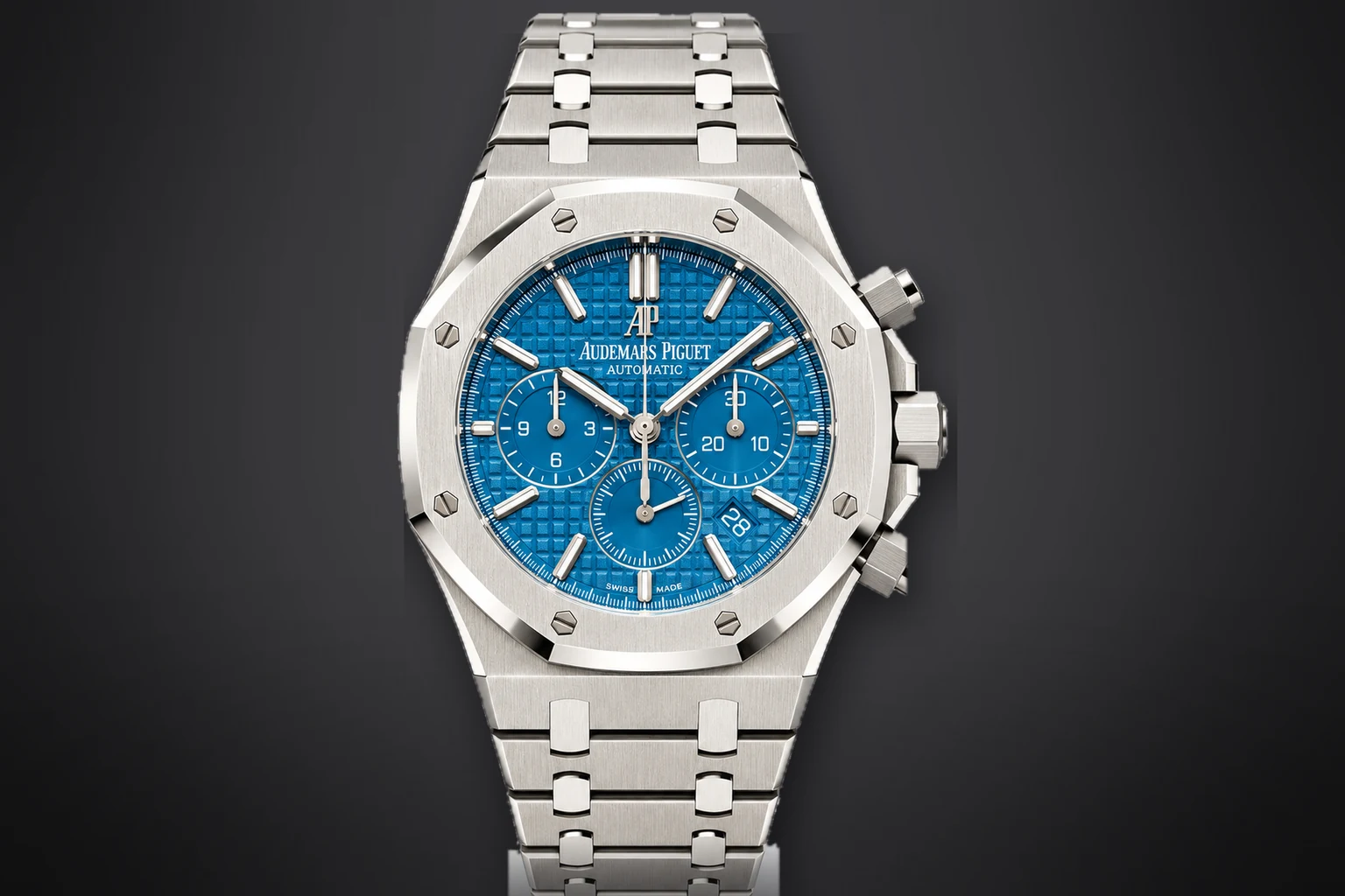 A steel Audemars Piguet Royal Oak Selfwinding Chronograph with a blue tapisserie dial and an integrated steel bracelet, lit against a dark ground