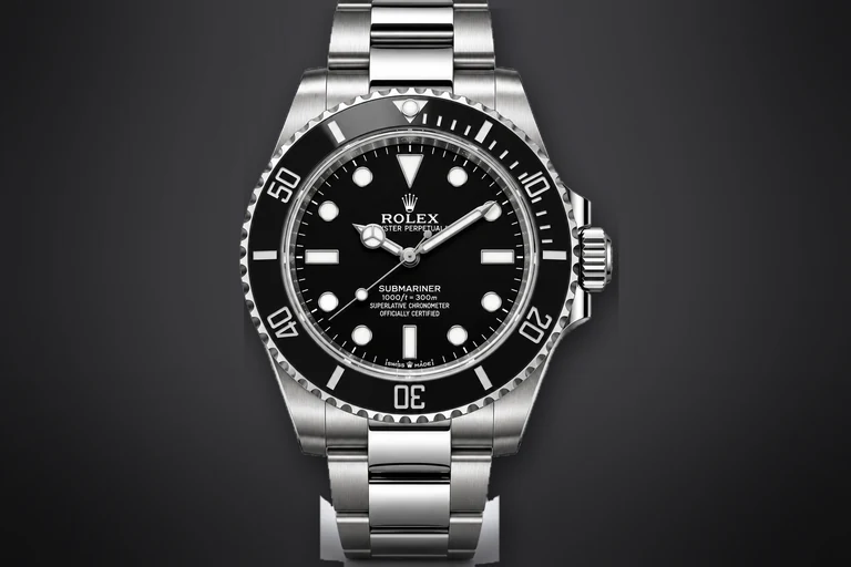 A steel Rolex Submariner with a black dial and black ceramic bezel on a steel Oyster bracelet, lit against a dark ground