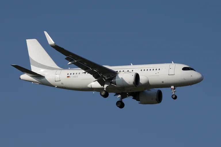 An Airbus ACJ319neo in white with a soft grey tail flash and sharklets on approach against a clean deep blue sky, three-quarter from the front.