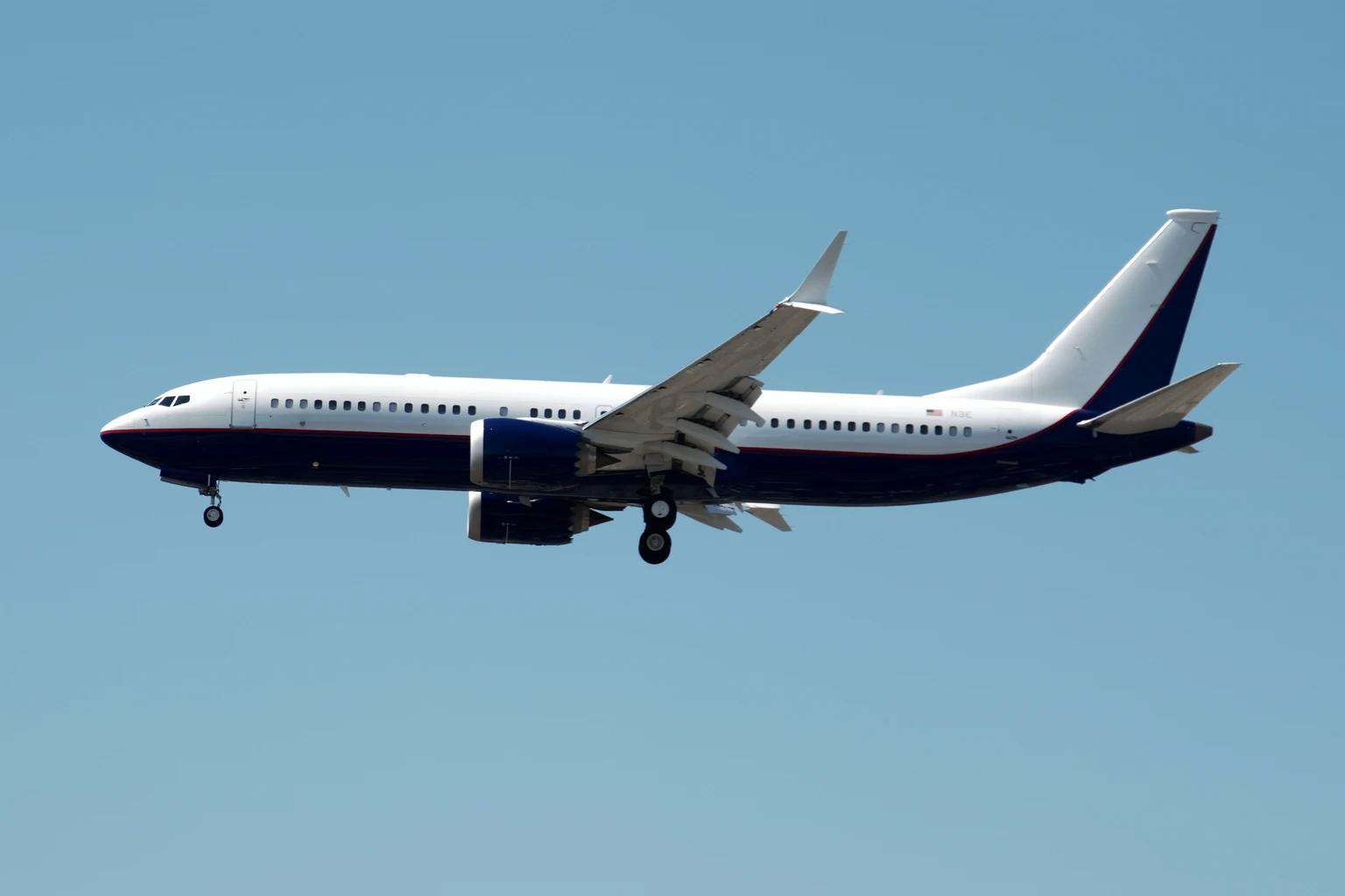 Stand-in photograph, not a MAX 7: a privately owned Boeing BBJ MAX 8, the longer sister of the BBJ MAX 7, white with a navy belly and tail, wings-level on final approach at Los Angeles.