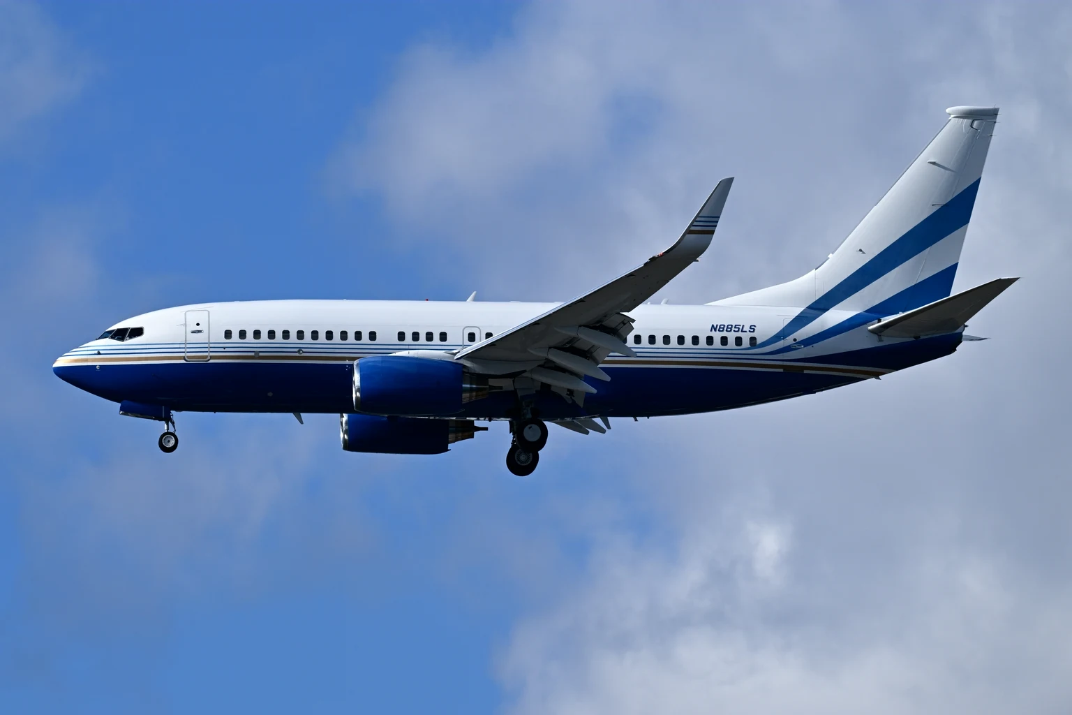 A white and royal-blue BBJ with a striped tail on final approach against a blue sky with soft cloud.