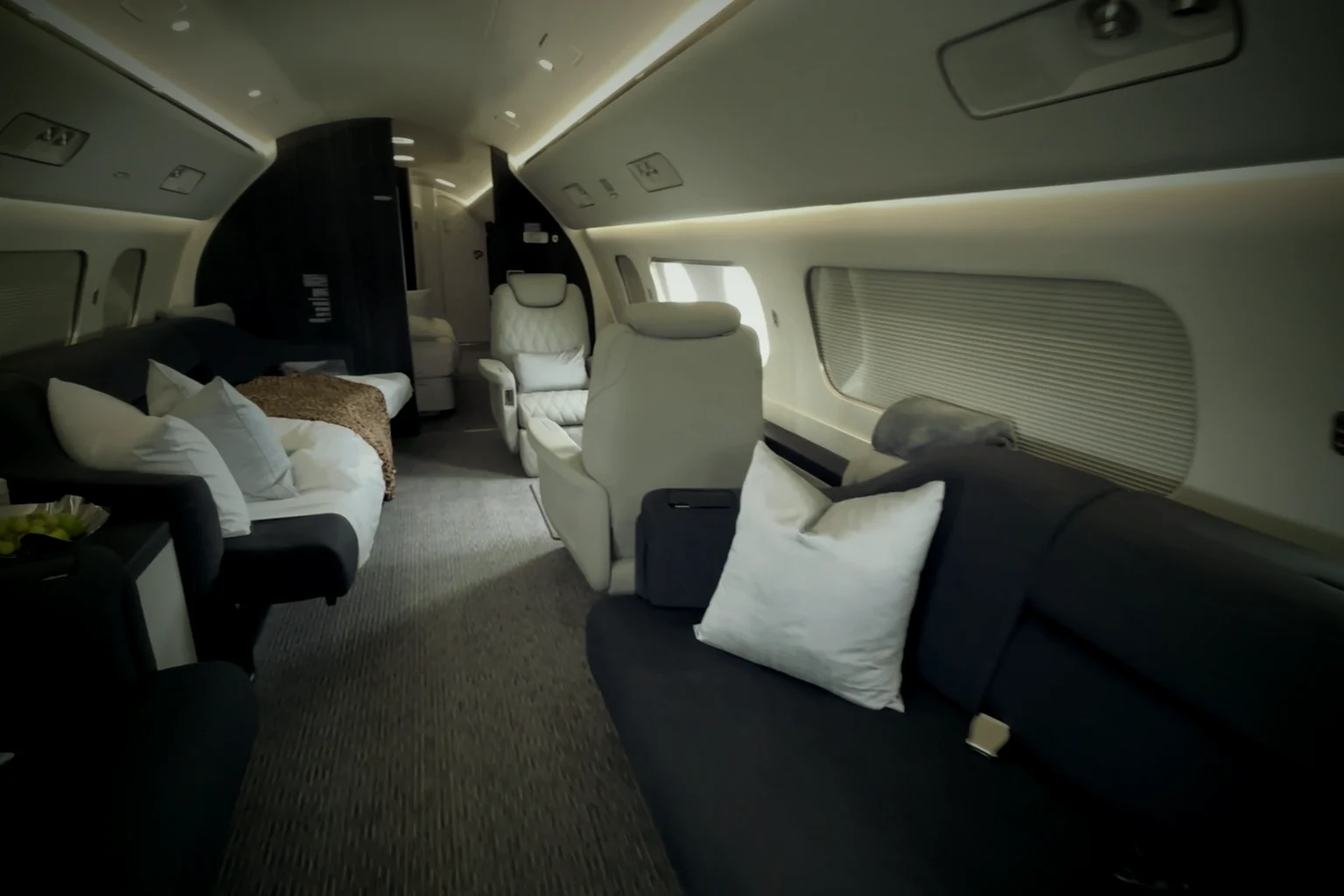 A private jet lounge with two divans made up as beds, white cushions, a bowl of grapes and cream club seats further aft.