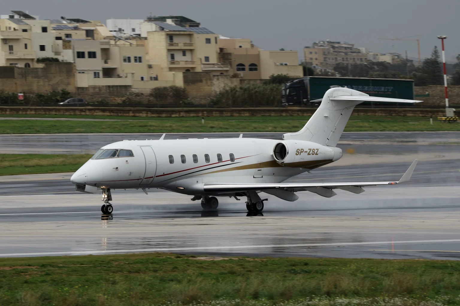 A white Bombardier Challenger 350 rolling along a wet runway under a grey sky
