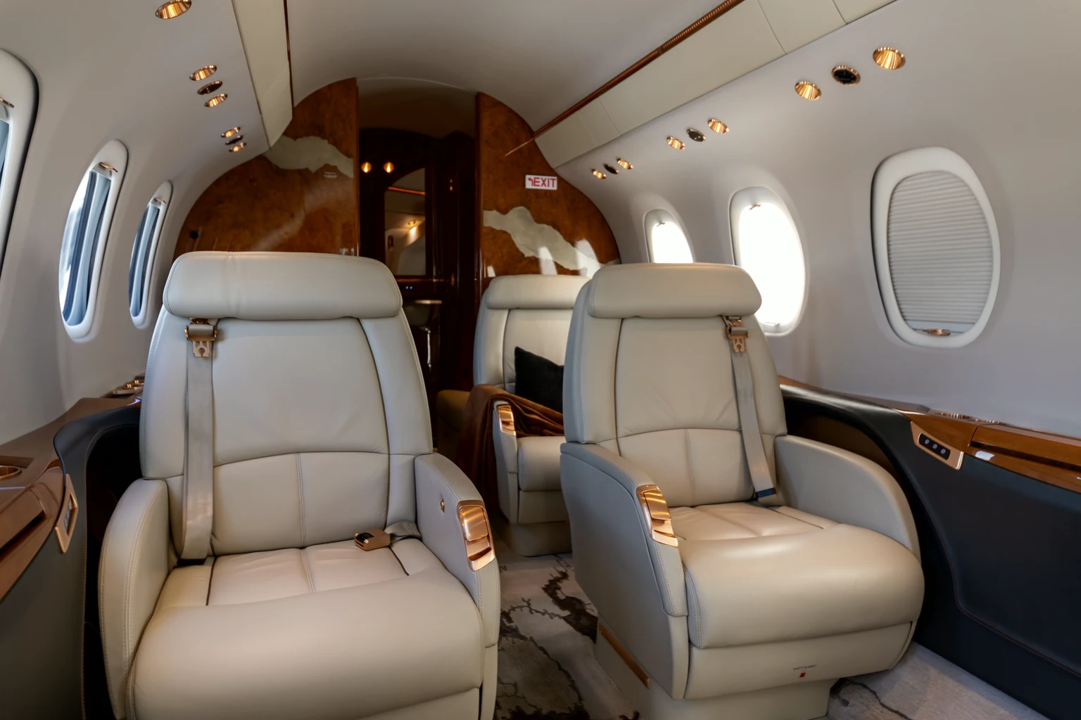 Two cream leather club seats facing forward in a Citation Latitude cabin, burl-wood bulkhead behind and bright window light.