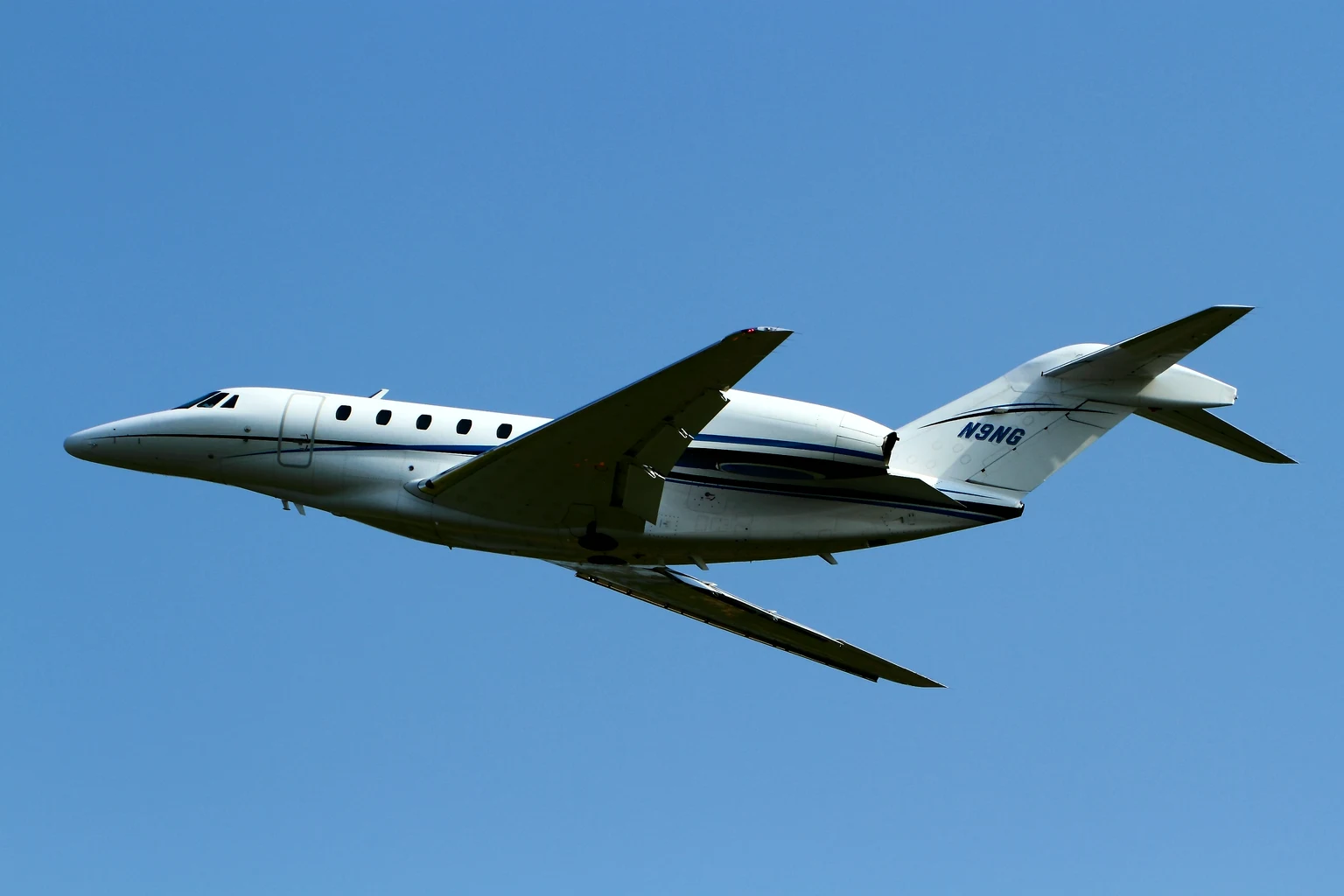 A white Citation X, the model the X+ developed from, with a blue cheatline flying past against a bright blue sky.