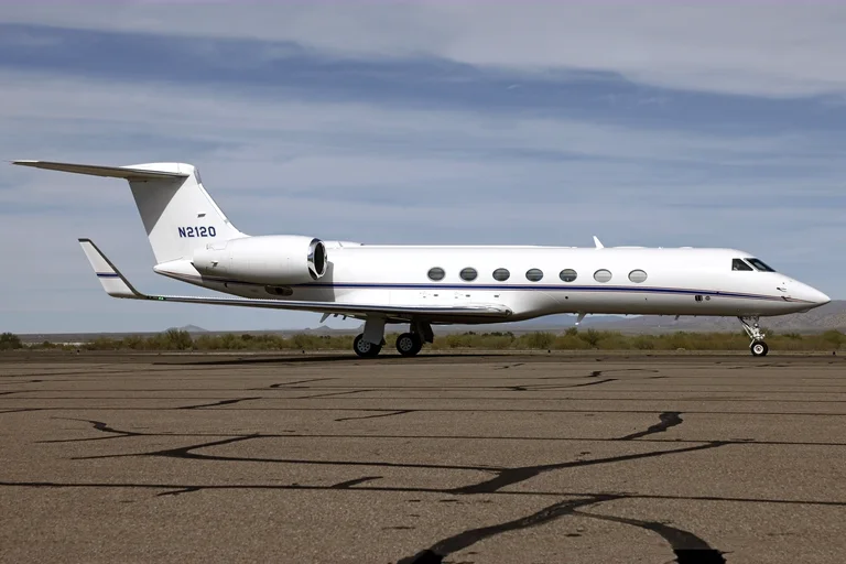 A white Gulfstream G550 with a blue and red cheatline taxiing side-on at Marana, Arizona, under a pale blue sky with desert hills behind.