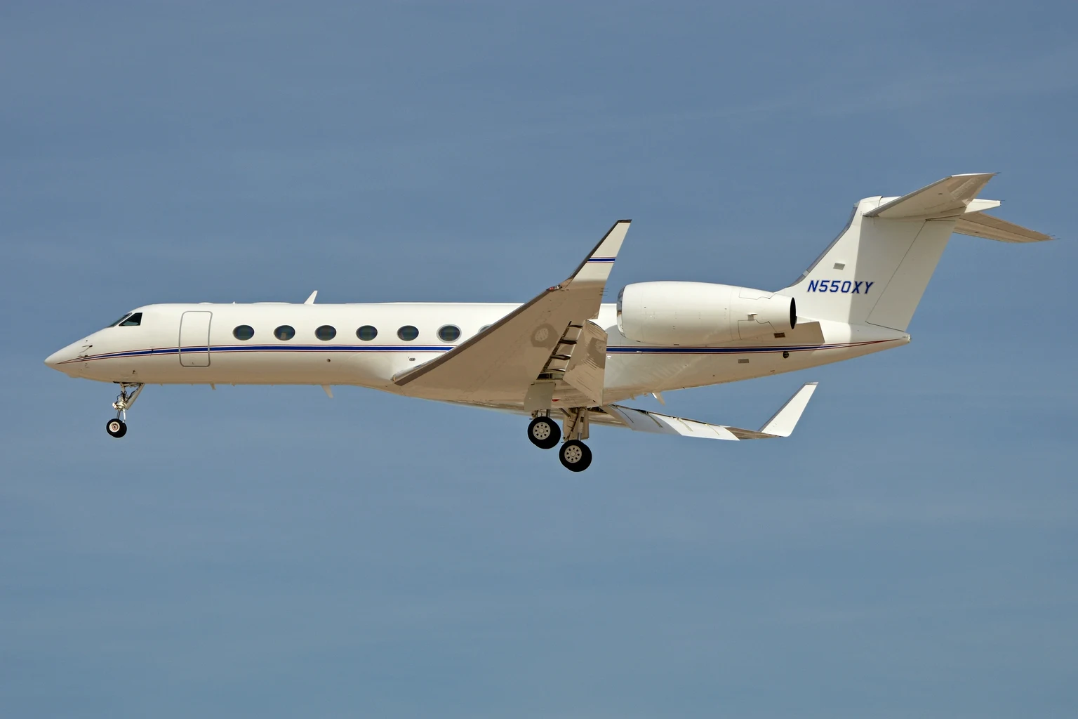 A white G550 with a blue cheatline on approach to Las Vegas against a clear blue sky, gear down.