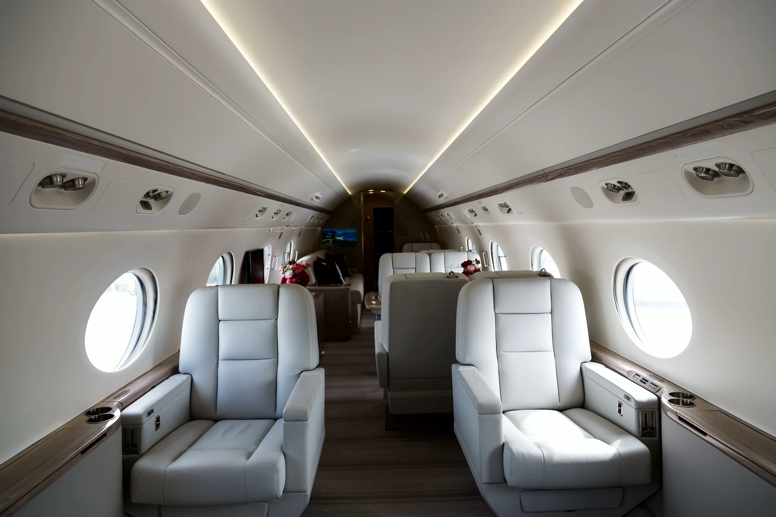 Looking down the aisle of a G550 cabin: cream leather club seats, large oval windows, flowers on a side ledge and a divan with dark red cushions further back.