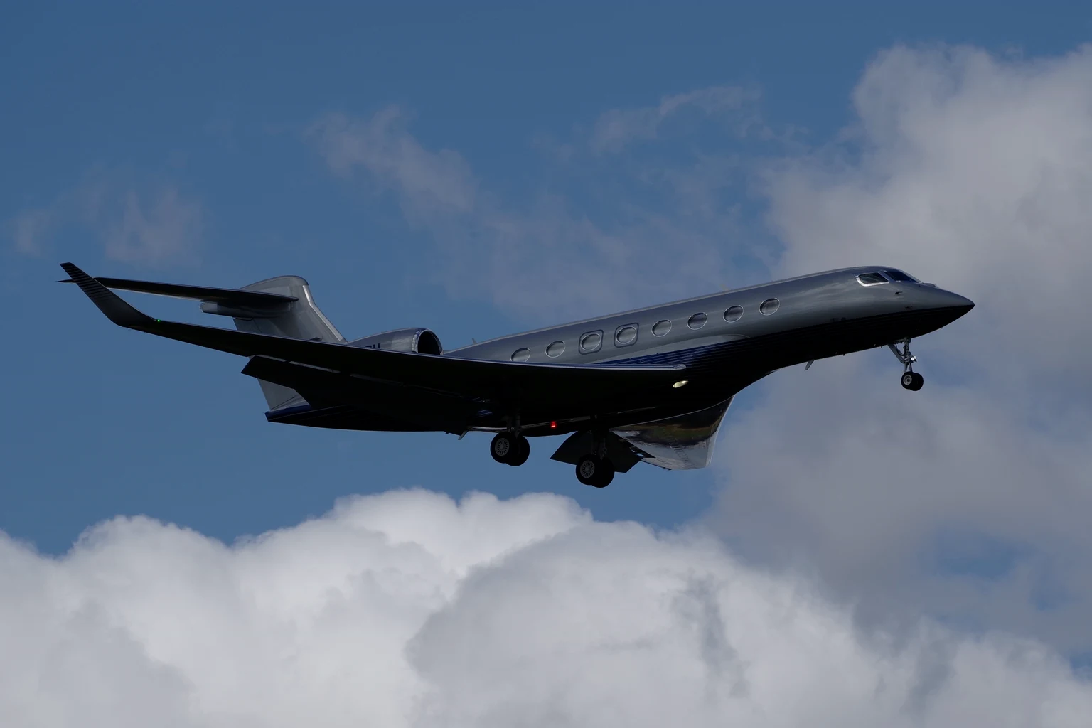 A silver-charcoal G650 with a black belly climbing against blue sky and white cumulus.