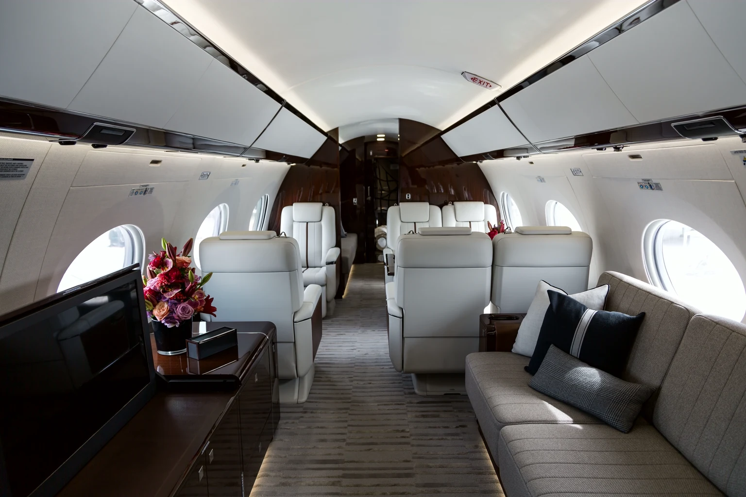 The full length of a G650 cabin: cream leather club seats, a divan with dark cushions, a vase of flowers and dark gloss wood.