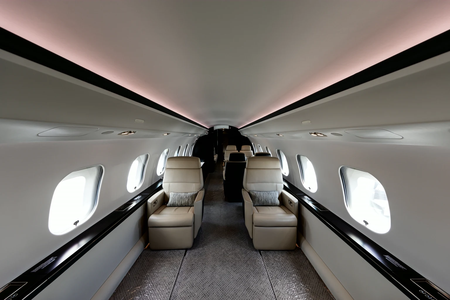 Looking down the aisle of a Global 6000 cabin between cream leather club seats, black cabinetry and a soft pink cove light.
