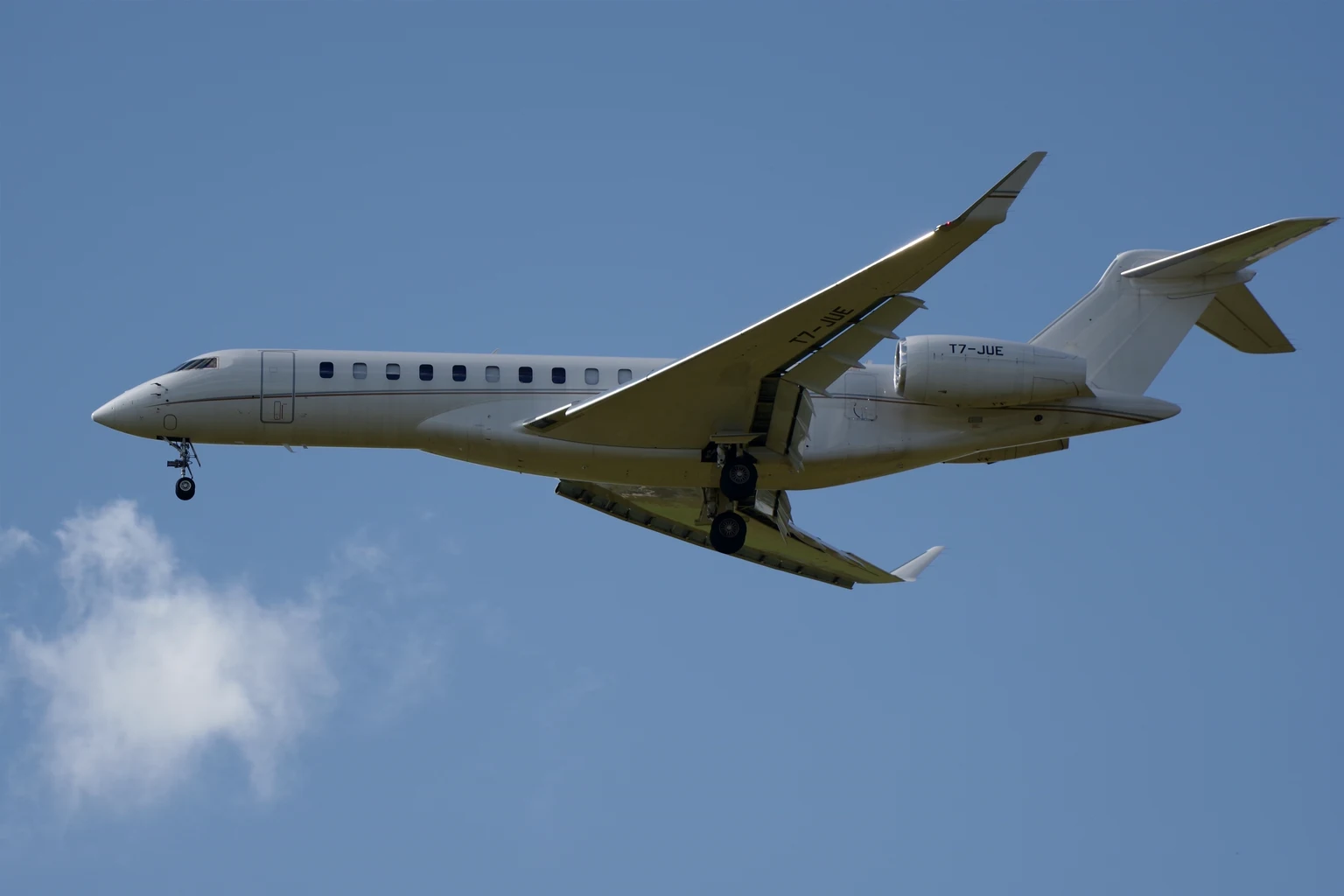 A plain white Global 7500 on approach against a blue sky, side-on from below.