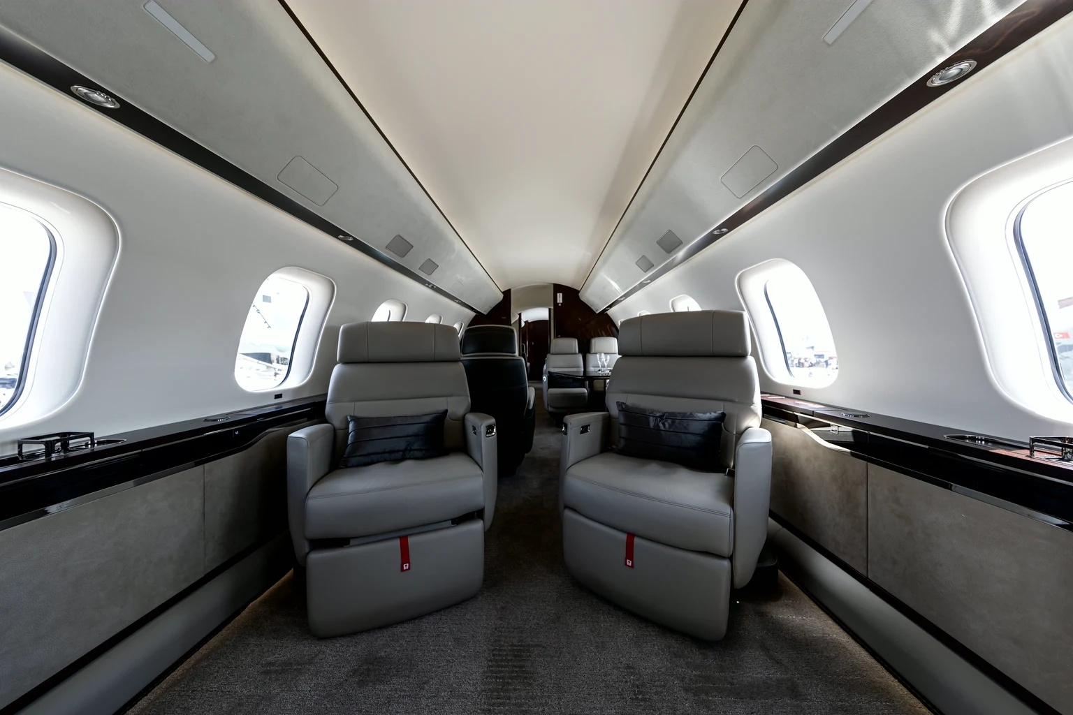 Two grey leather club seats facing forward in a Global 7500, black cushions, large windows and the cabin running on behind.