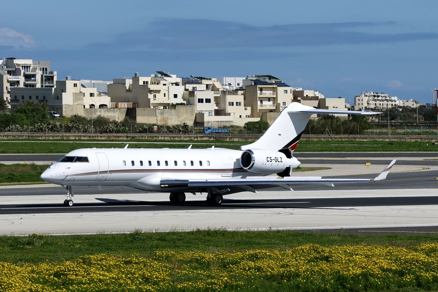 A white Bombardier Global long-range business jet lined up on a runway on a clear day