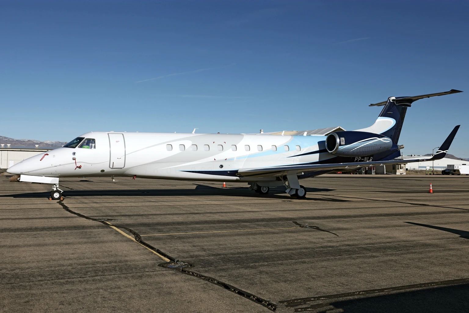 An Embraer Legacy 650 in white with pale-blue and navy sweeps parked on a sunlit apron at Kingman, Arizona, under a clear blue sky.
