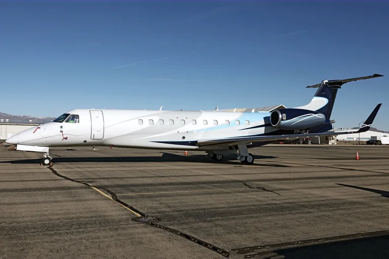 An Embraer Legacy 650 in white with pale-blue and navy sweeps parked on a sunlit apron at Kingman, Arizona, under a clear blue sky.