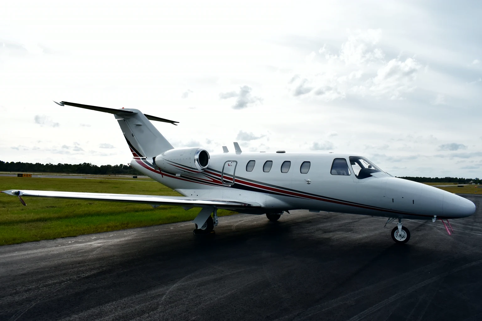 A white Cessna Citation light jet with red pinstripes parked on a wet apron under a cloudy sky