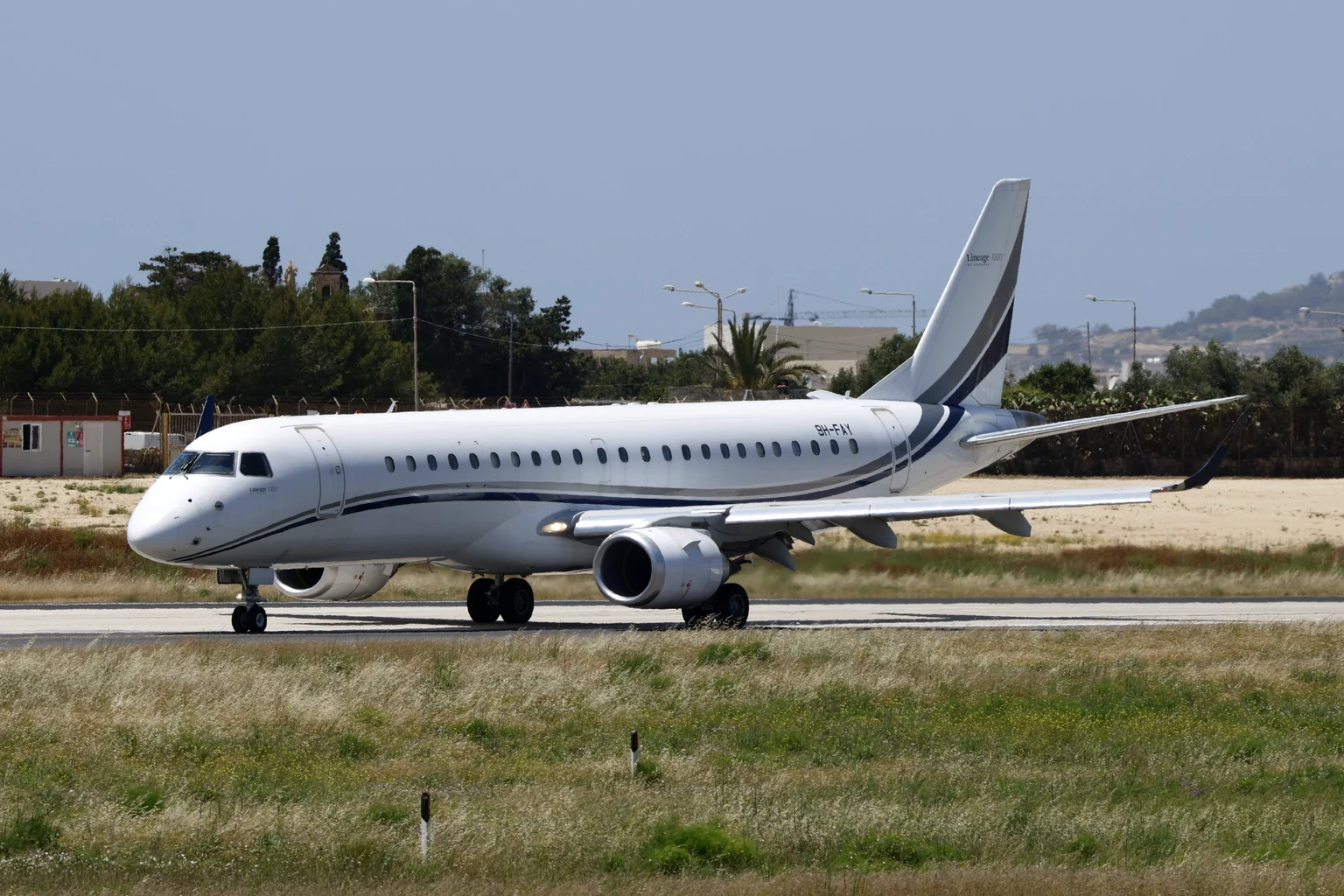 An Embraer Lineage business airliner in white and blue taxiing along a runway