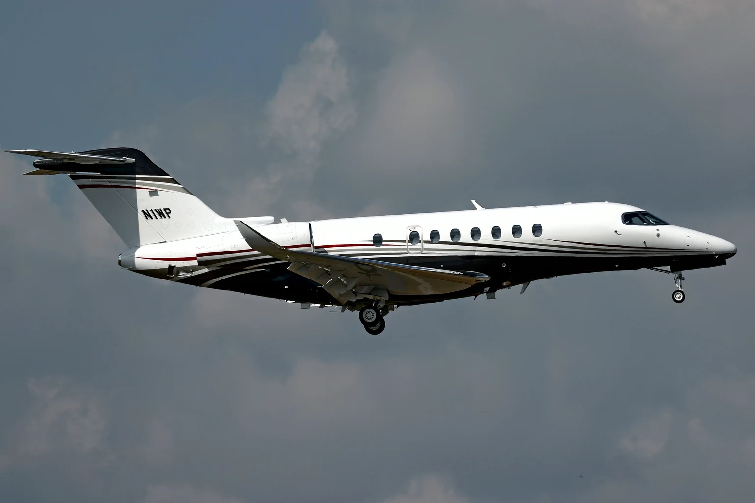 A white Cessna Citation Longitude with a black and red sweep on approach under grey-blue cloud