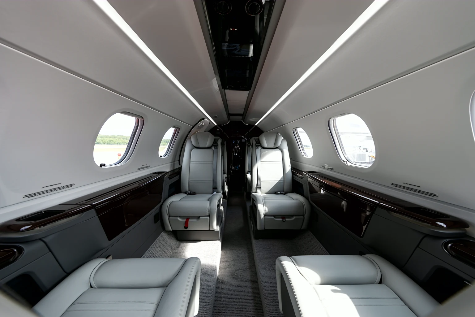 Looking down the aisle of a Phenom 300 cabin: pale grey leather club seats, gloss black side ledges and oval windows.