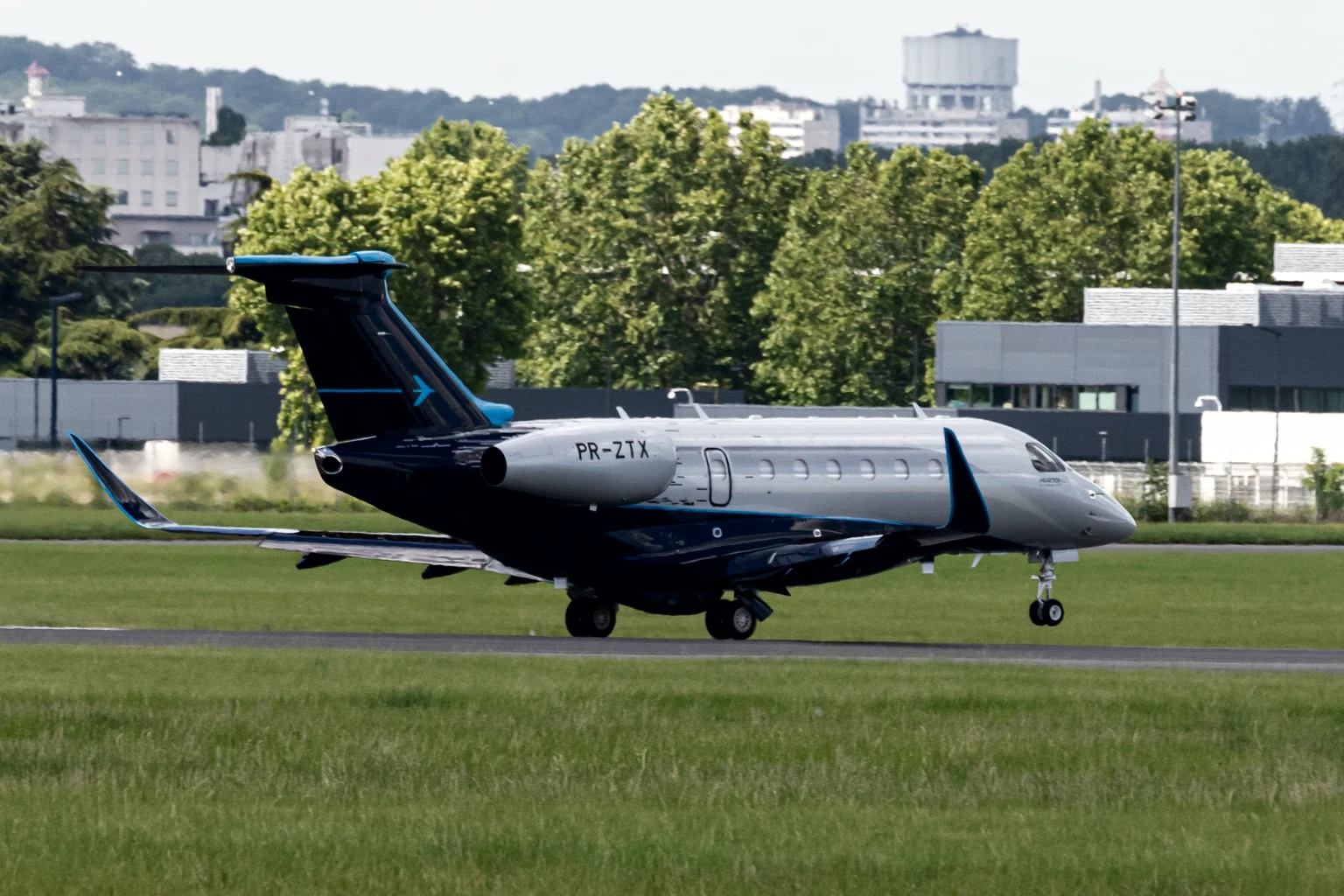 Embraer's own Praetor 600 in navy and silver touching down wings-level at Le Bourget, green trees behind.