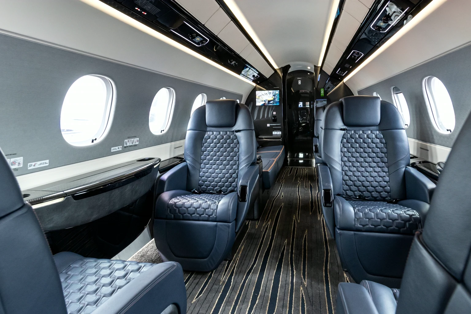 Looking down a Praetor 600 aisle between navy quilted leather club seats, round windows either side.