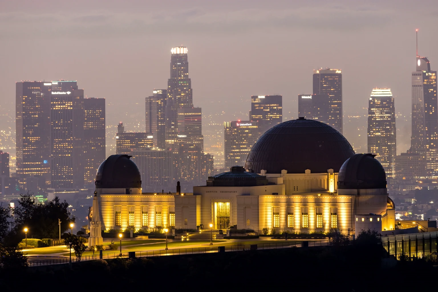 Griffith Observatory lit at dusk with the downtown skyline behind