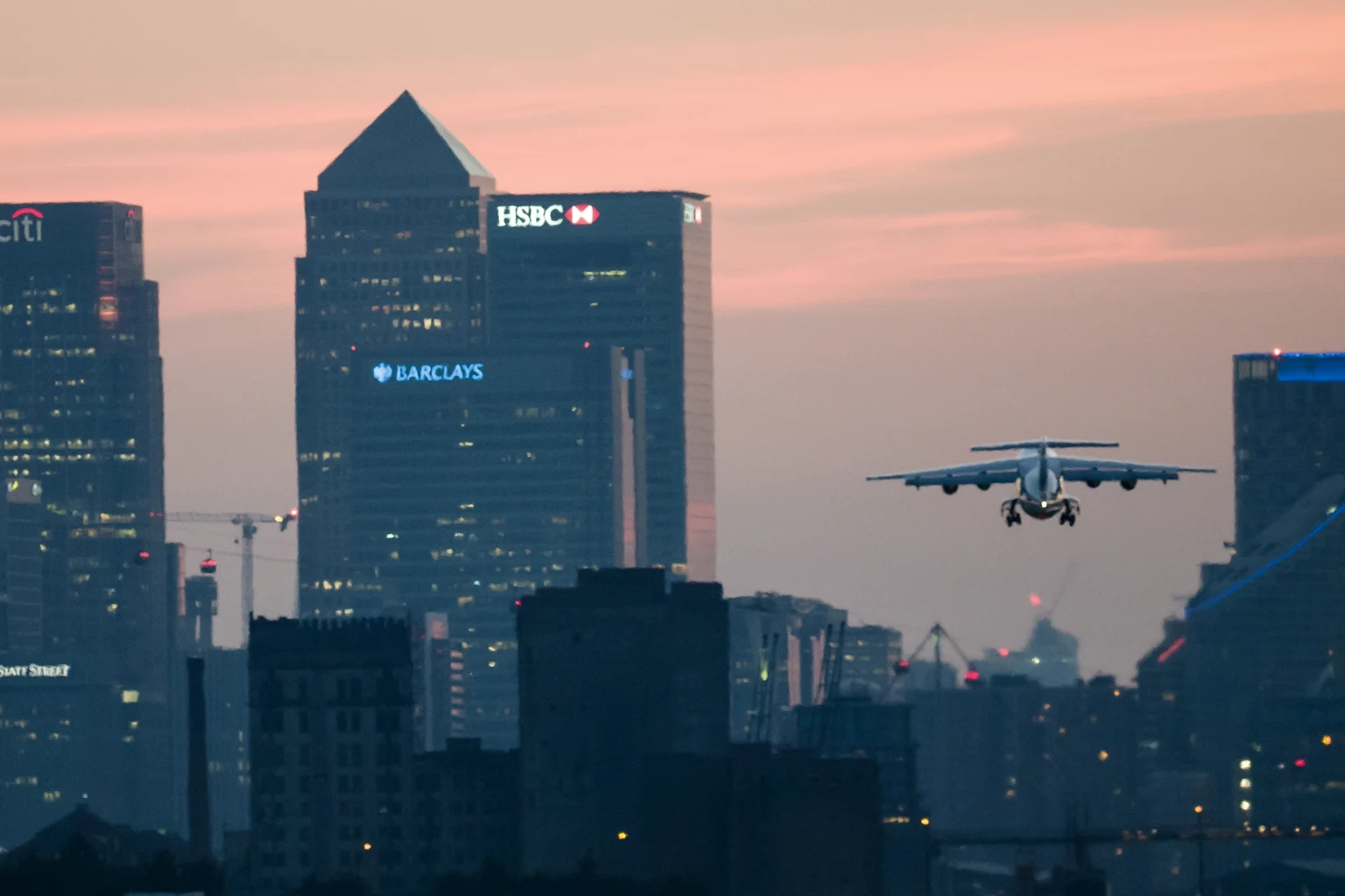 An aircraft on approach to London City Airport at sunset, Canary Wharf's towers behind