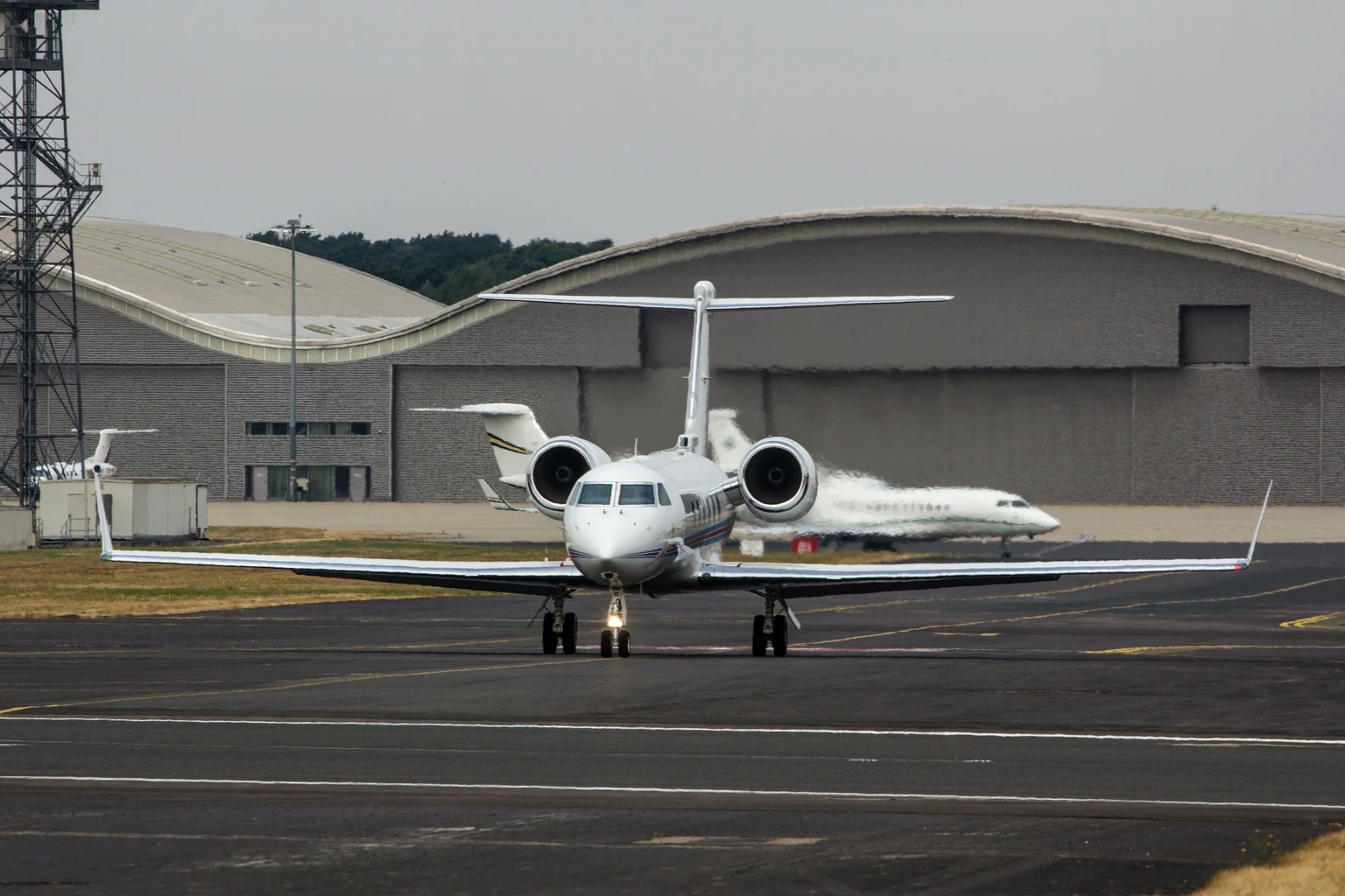 A Gulfstream G450 taxiing towards the camera in front of Farnborough's curved hangars