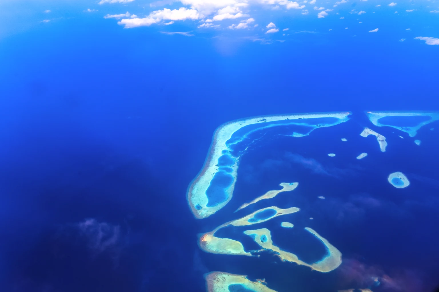 An aerial view of a Maldivian atoll, reef and lagoon in deep blue water