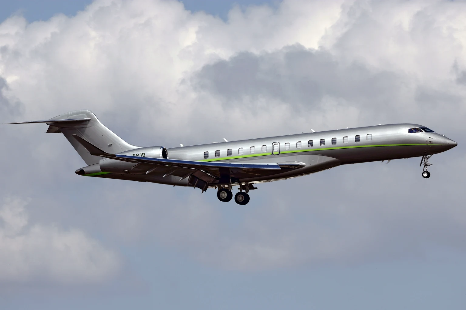 A silver Bombardier Global 8000 on approach under cumulus