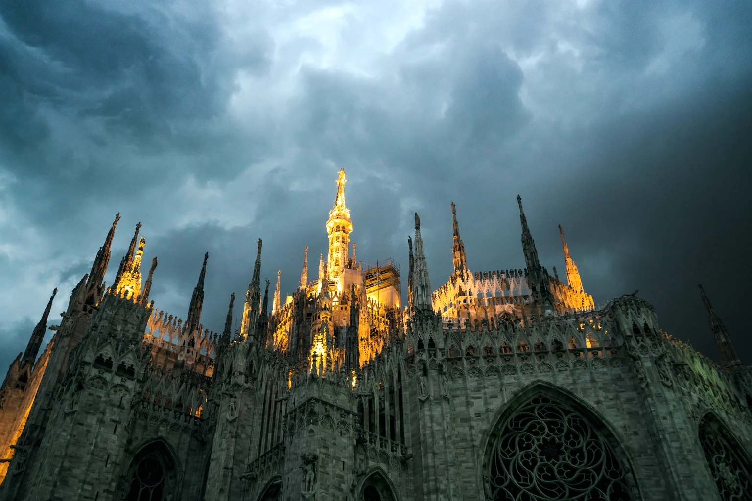 The spires of the Duomo in Milan lit under a stormy sky