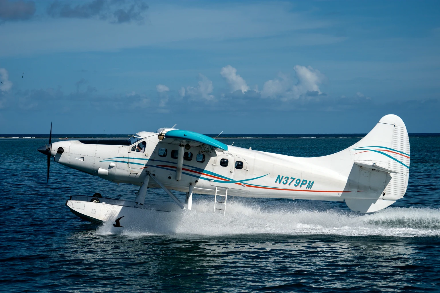 A turbine Otter on floats lifting off turquoise water in a sheet of spray