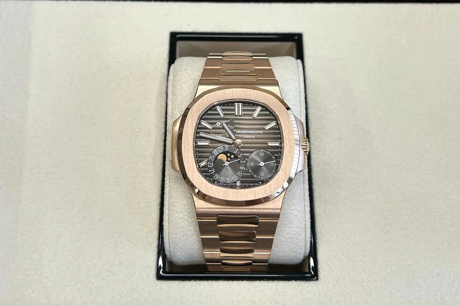 A rose-gold Patek Philippe Nautilus 5712 with a brown dial, moon phase and power reserve, on its cushion inside its open presentation box
