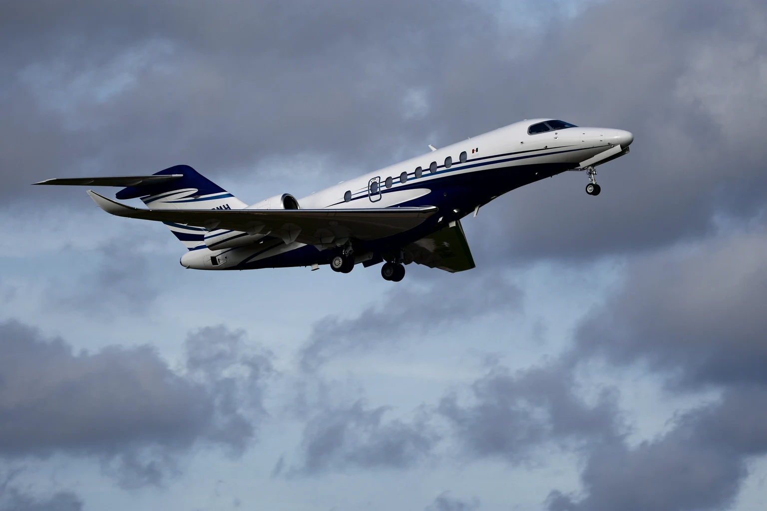 A private jet climbing away through broken cloud with its gear still down