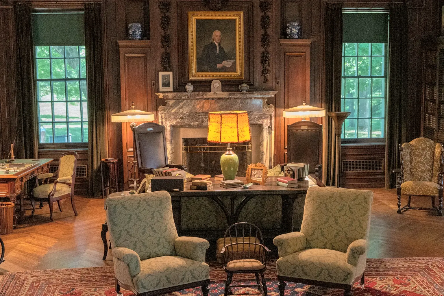 A wood-panelled private study with a desk, lamps and armchairs by the fireplace